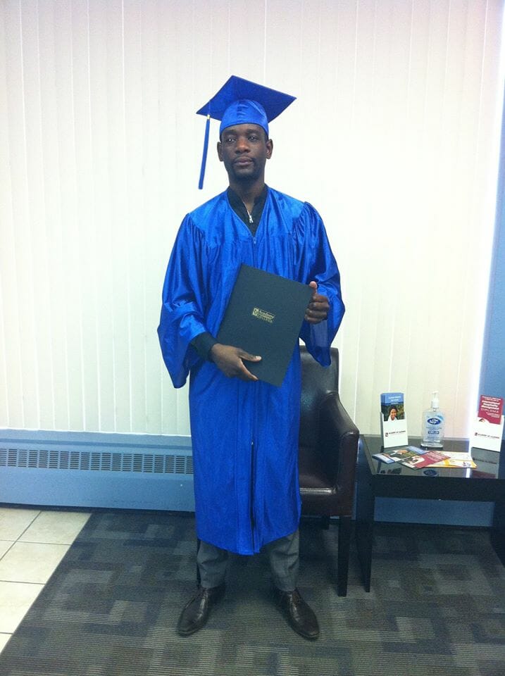 Graduate wearing a blue cap and gown holding a diploma folder during a graduation ceremony.
