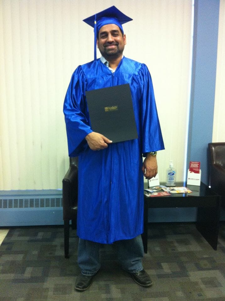Male graduate in blue cap and gown holding diploma during graduation ceremony.