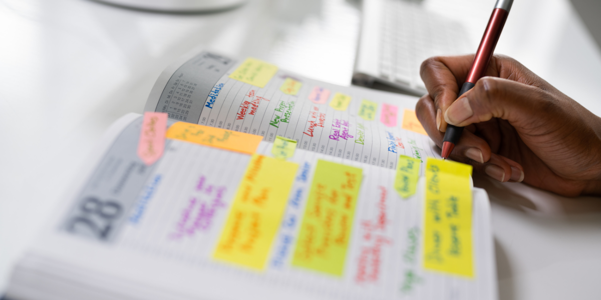 A person writing a daily schedule on a planner, emphasizing time management during unemployment.