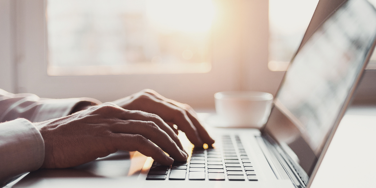 Side view of hands typing on laptop keyboard in warm-lit workspace with coffee cup nearby, representing the flexibility of Microsoft Office 365 for remote work capabilities.