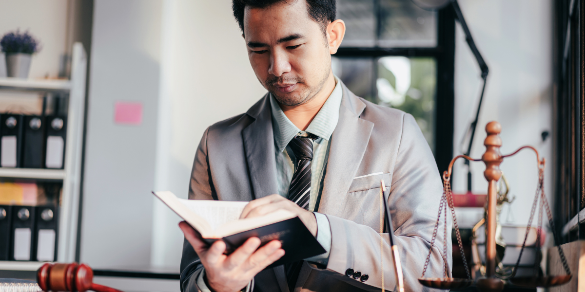 Law clerk conducting legal research with law books and scales of justice on desk, demonstrating technical research skills required for legal assistant positions